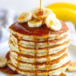 Thick and fluffy banana pancakes topped with syrup and sliced bananas